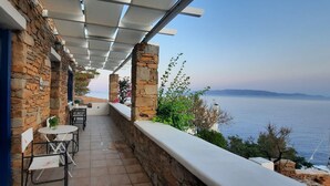 A stone building with a covered outdoor seating area overlooking a body of water.