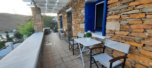 A stone building with a balcony, white tables and chairs, and a blue door. - Cycladic House with a Pool. Exceptional views and 2min walk from the beach. (Kythnos)