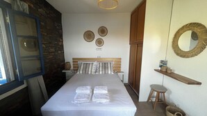 A bedroom with a bed, a wooden headboard, a bedside table, a nightstand, a mirror, a shelf with decorative items, and a woven basket.