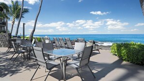 An outdoor seating area with a glass table and chairs, overlooking the ocean. - Kona Makai #5203 Ocean View , 
A Hawaiian Paradise (Kailua-Kona)