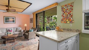A kitchen with a granite countertop, white cabinets, and a view of a balcony with plants. - Kona Makai #5203 Ocean View , 
A Hawaiian Paradise (Kailua-Kona)