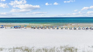 Ein Strand mit weißem Sand, klarem blauen Wasser und einer Reihe blauer und weißer Strandsonnenschirme.