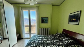 A bedroom with a bed, a radiator, a window with a view of mountains, and a ceiling fan.