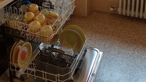 A kitchen with a dish rack full of dishes, a stove, and a window with a curtain.