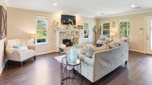A spacious living room with a fireplace, a sofa, a coffee table, and a TV mounted on the wall. - The Vine - Elegant "Wild Rose" Cottage on Vineyard with Private Lake, Sleeps 4 (New Ulm)