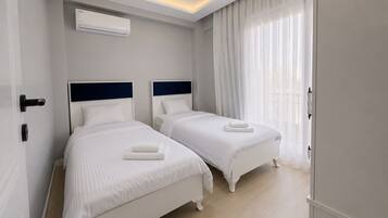 A hotel room with two beds, a ceiling light, an air conditioning unit, and a large window with sheer curtains.