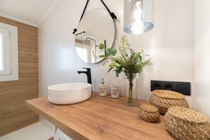A modern bathroom with a wooden vanity, a large mirror, a white sink, and a small potted plant.