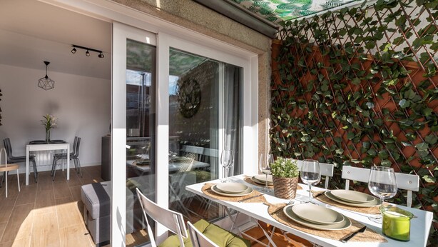 Un comedor con una mesa preparada para dos, un ventanal corredero que da a un espacio exterior y una pared cubierta de plantas trepadoras.