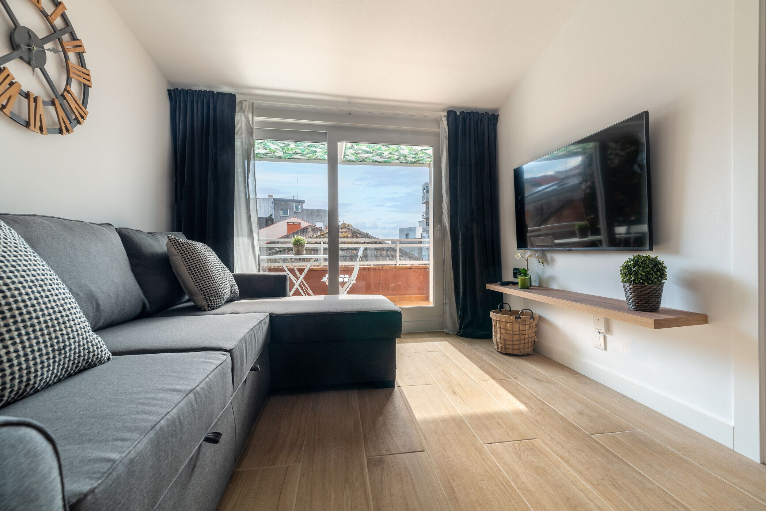Een moderne woonkamer met een grijze bank, een flatscreen televisie aan de muur en een houten vloer.
