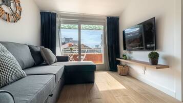 Een moderne woonkamer met een grijze bank, een flatscreen televisie aan de muur en een houten vloer.