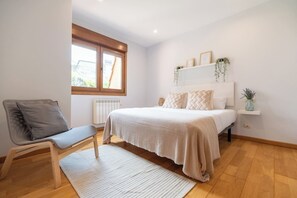 A bedroom with a bed, a chair, a window, and a radiator. - Combarro Beach Blue (Poio)