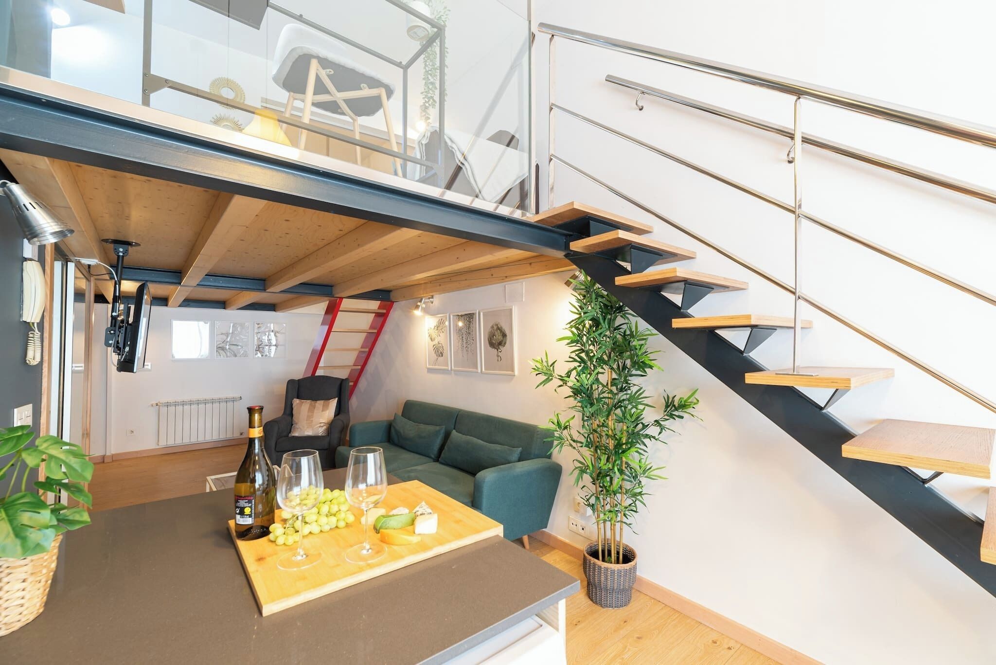 Een modern interieur met een houten eettafel gedekt met eten en drinken, een groene bank, een trap met een metalen leuning en een potplant.