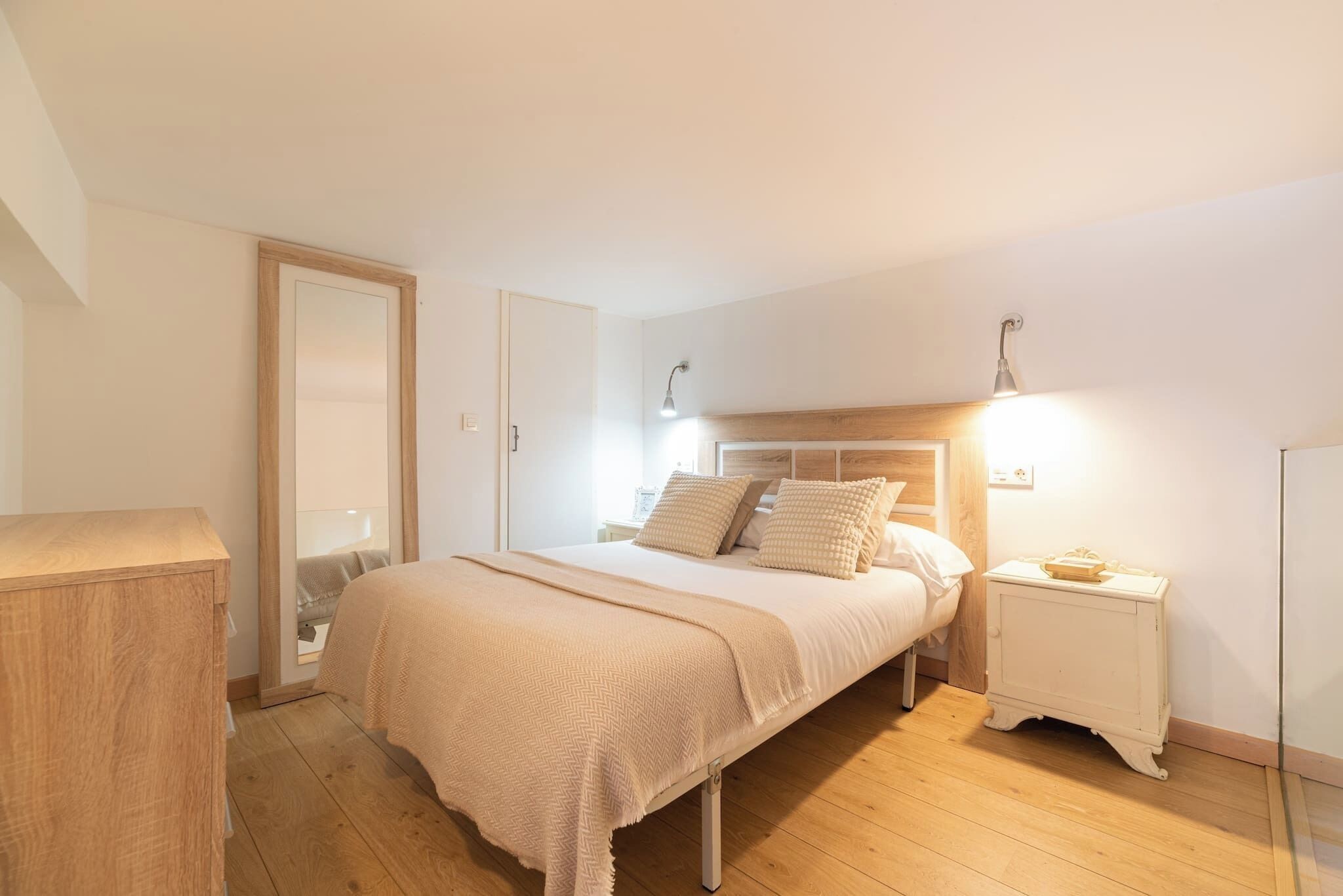 A bedroom with a bed, bedside table, lamp, and wooden floor.