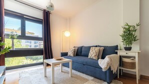 Un salon avec un canapé, une petite table, une lampe, une plante en pot et une vue sur les bâtiments à l’extérieur.