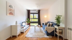 Un salon moderne avec un canapé bleu, des meubles blancs, un tapis blanc et une grande fenêtre avec des rideaux.