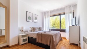 Une chambre à coucher avec un lit, une table de chevet, une lampe et une fenêtre avec des rideaux.