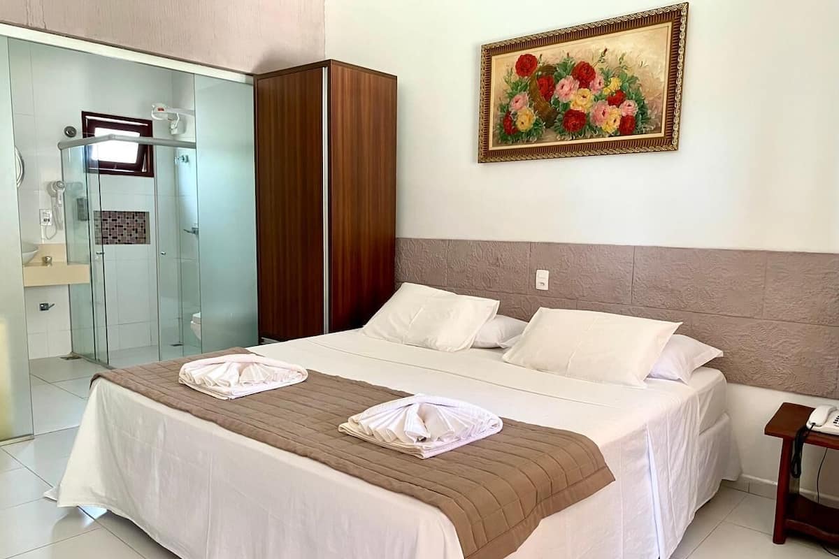 A hotel room with a bed, a wardrobe, a shower, and a painting on the wall.