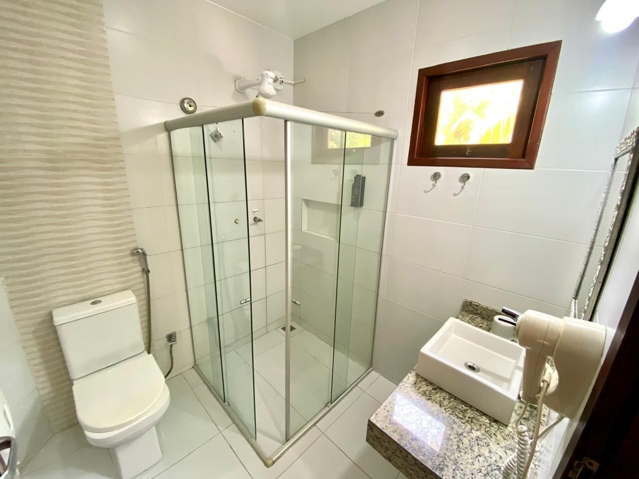 Casa de banho com cabine de duche em vidro, sanita e lavatório com barra para toalhas.