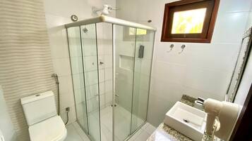 Casa de banho com cabine de duche em vidro, sanita e lavatório com barra para toalhas.