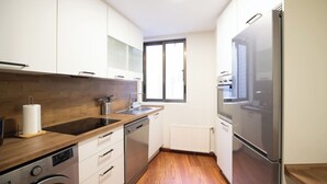 Una cocina compacta con armarios blancos, lavavajillas de acero inoxidable, horno empotrado y un refrigerador grande.
