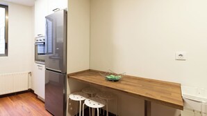 Una cocina compacta con un refrigerador de acero inoxidable, un horno empotrado y una encimera de madera. Hay tres taburetes blancos debajo de la encimera.