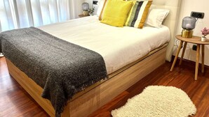 A neatly made bed with a white headboard, a grey throw blanket, and multiple pillows in yellow, green, and black. - Olive Apartment with Parking (Vigo)