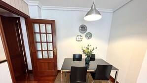 A dining area with a wooden door, a table with chairs, a vase with flowers, and a pendant light. - Olive Apartment with Parking (Vigo)