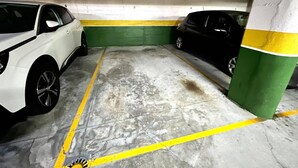 A parking garage with two cars parked, concrete floor, yellow lines, and green and white painted walls. - Olive Apartment with Parking (Vigo)