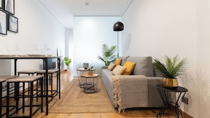 A modern living room with a grey sofa, a coffee table, and a dining area with stools and a table set for four. - Precioso Loft Puerto Maritimo with Parking (Vigo)