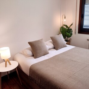 Un lit bien fait, avec une couverture et des oreillers de couleur beige, une lampe de chevet et une plante en pot.