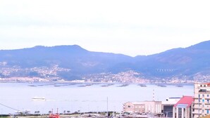 A coastal city with a marina, buildings, and mountains in the background.