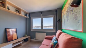 Ett vardagsrum med en rosa soffa, en tv på ett träställ, en världskarta på väggen och ett fönster med utsikt över kullar.