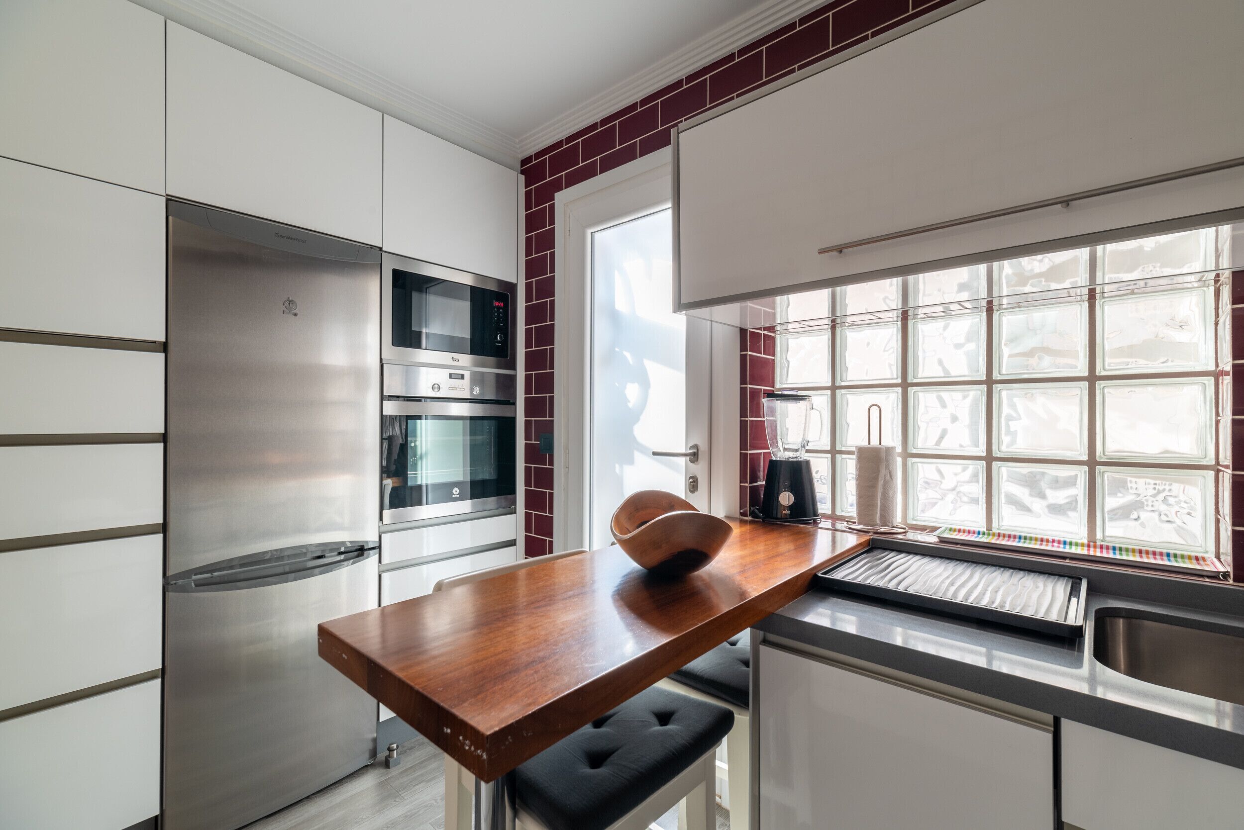A modern kitchen with stainless steel appliances, a wooden countertop, and a window with a view.