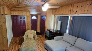 Ein Zimmer mit Holzwänden, einer Couch, einem Sessel, einem Tisch mit Lampe und einem Deckenventilator.
