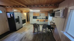 Eine kleine Küche mit Holzausstattung, einem Kühlschrank, einer Mikrowelle und einem Essbereich mit Tisch und Stühlen.