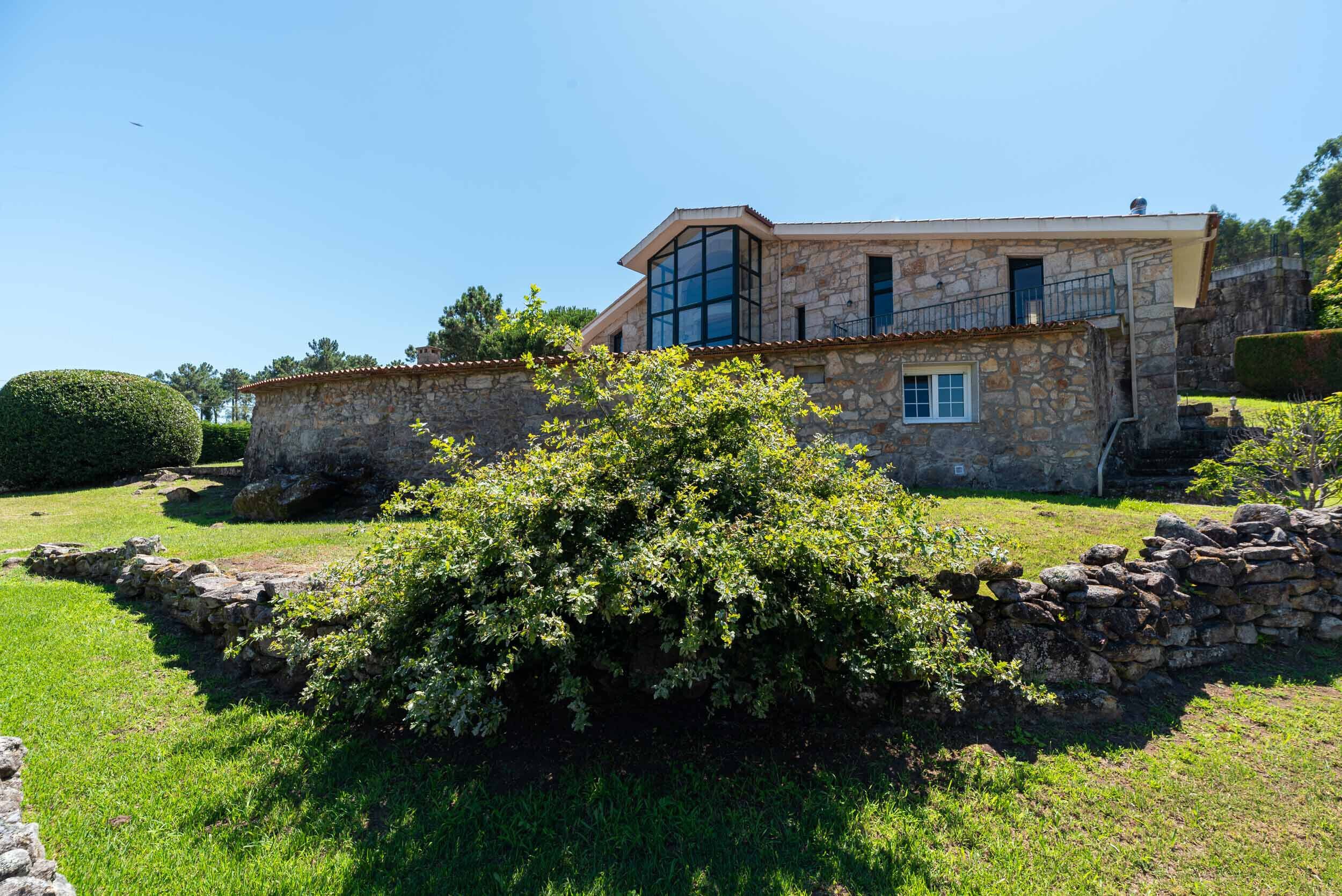 Una casa de piedra con un amplio ventanal y un muro de piedra.