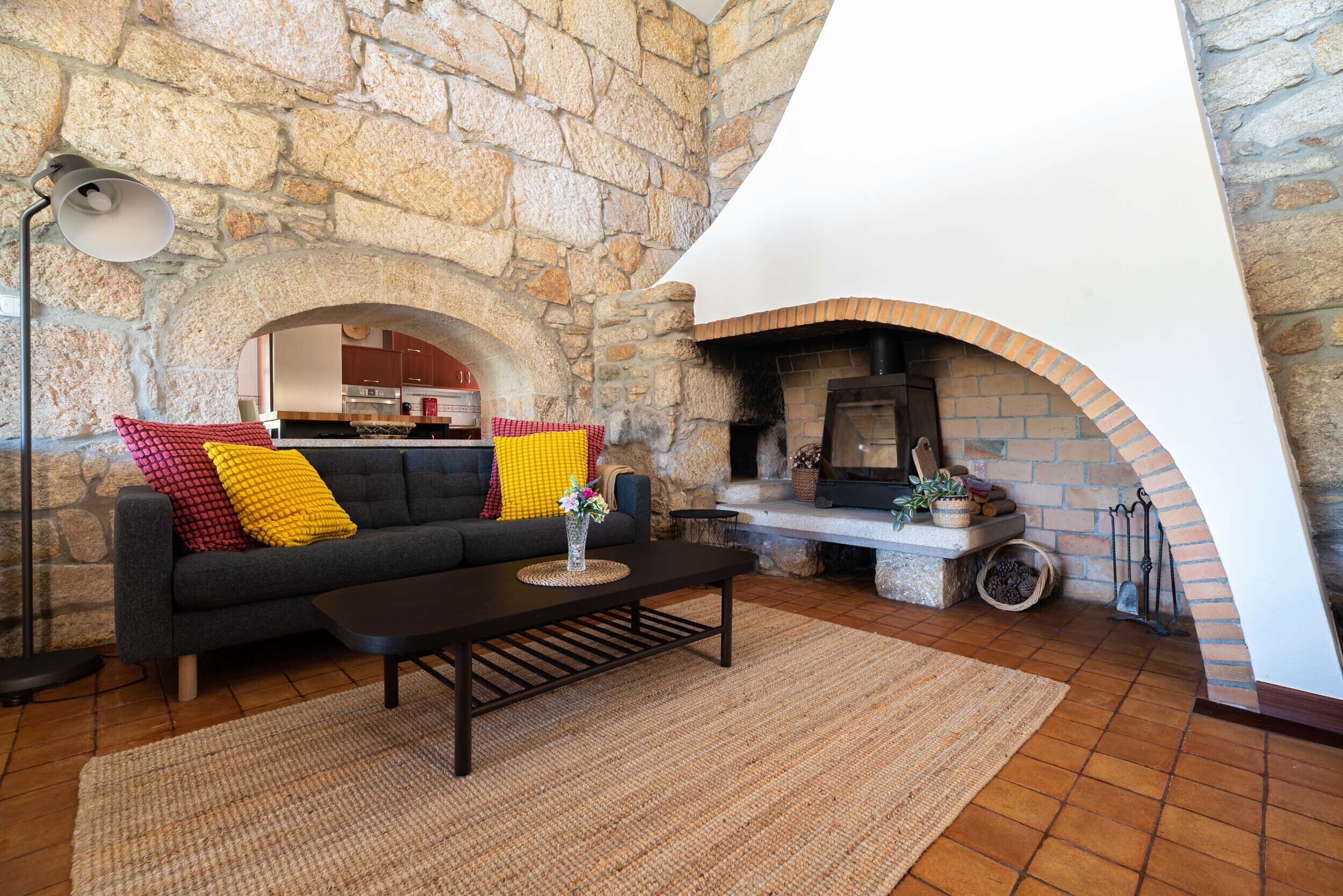 A cozy living room with a stone wall, a fireplace, a sofa with colorful cushions, and a coffee table.