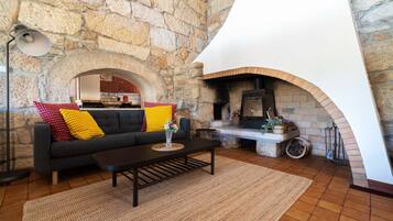 A cozy living room with a stone wall, a fireplace, a sofa with colorful cushions, and a coffee table.