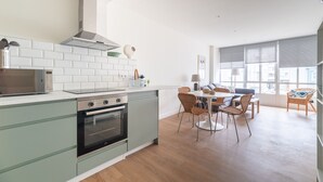 Cocina moderna con azulejos blancos tipo metro, campana extractora de acero inoxidable y horno empotrado. Cuenta con un comedor con mesa y sillas, y ventanas amplias que ofrecen luz natural.