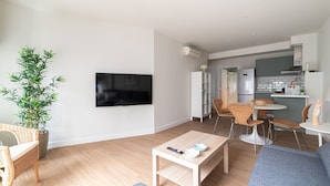 Una sala de estar moderna con un televisor de pantalla plana, un comedor con sillas de mimbre y una cocina al fondo.