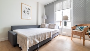 Un dormitorio con cama, una silla, ventana con vistas y un cuadro en la pared.