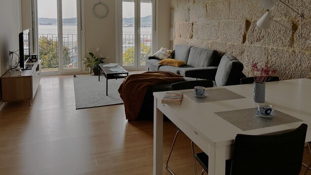 Uma sala de estar moderna com sofá, mesa de jantar e vista da cidade através de amplas janelas.