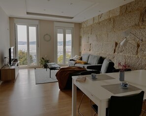 A modern living room with a sofa, a dining table, and a view of the city through large windows.