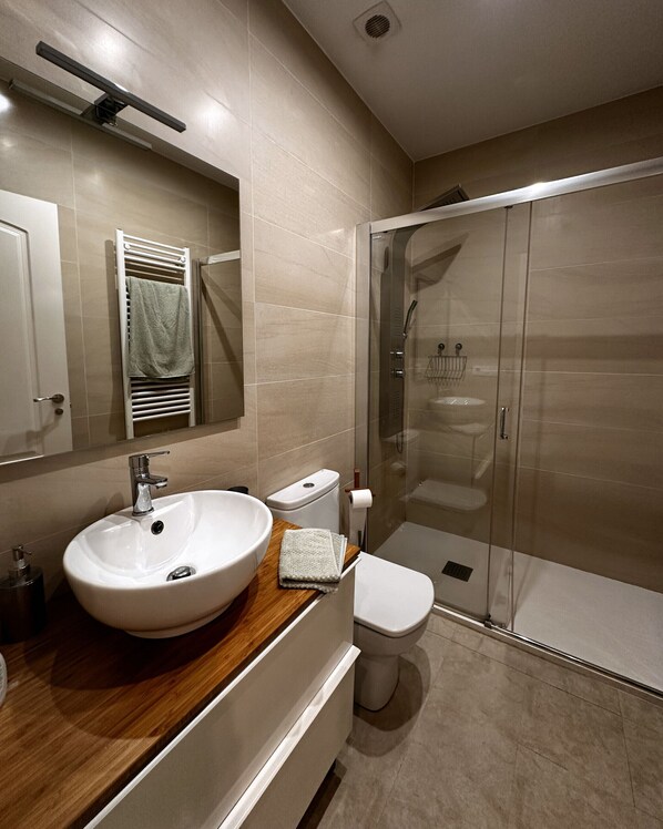 A modern bathroom with a large sink, toilet, and glass-enclosed shower.