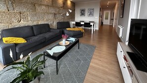 Uma sala de estar moderna com uma parede de destaque em pedra, um sofá, uma mesa de centro e uma televisão.