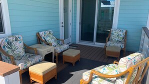 A covered outdoor seating area with wicker furniture and a sliding glass door leading to a balcony. - Nautical Nest in Fort Myers Beach (Fort Myers Beach)