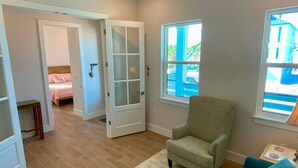 A room with a large window, a door leading to another room, and a chair. - Nautical Nest in Fort Myers Beach (Fort Myers Beach)