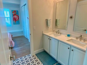 A bathroom with two sinks, a mirror, and a door leading to another room. - Nautical Nest in Fort Myers Beach (Fort Myers Beach)