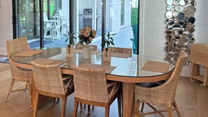 A dining area with a glass table, wicker chairs, a chandelier, and a wall-mounted mirror sculpture. - Beach Bum Luxury 30A, Heated Pool, Golf Cart, Bikes, 3 Minute Walk to The Beach! (Santa Rosa Beach)