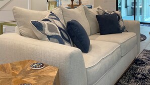 A modern living room with a staircase, a sofa with patterned cushions, a wooden coffee table, and decorative wall art. - Beach Bum Luxury 30A, Heated Pool, Golf Cart, Bikes, 3 Minute Walk to The Beach! (Santa Rosa Beach)